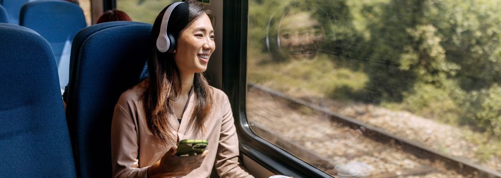 Mujer asiática en tren mirando por la ventanilla y escuchando música con cascos