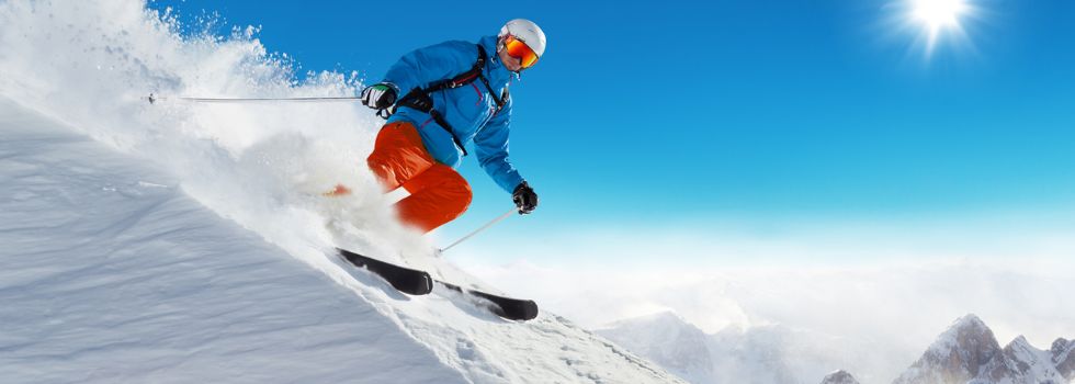 Esquiador bajando por una pista cubierta de nieve bajo un cielo azul