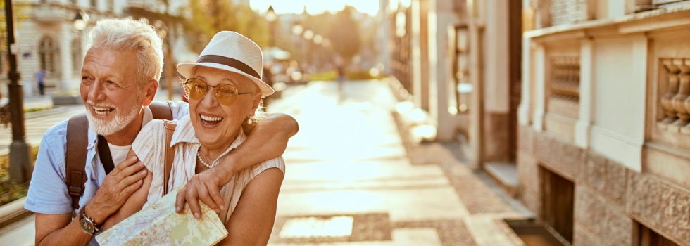 Pareja senior blanca abrazada por la calle. Ella lleva un mapa en las manos