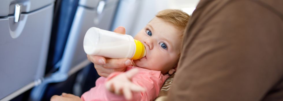 Bebé rubio con ojos azules tomando el biberón en un avión